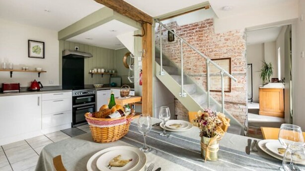 A modern kitchen with white cabinets, a red kettle, and a dining area with a marble table set for two.
