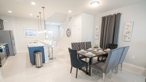 Una cocina moderna con una isla central, un comedor con una mesa redonda y sillas, y una escalera que conduce a un nivel superior.