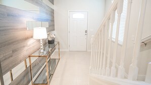 Un pasillo con pared de madera, una puerta blanca y una escalera con barandilla de balaustres blancos.