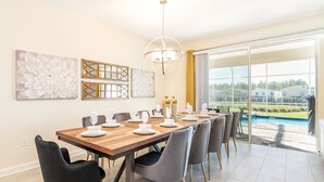 A dining area with a long wooden table, grey chairs, and a chandelier. - Last Minute Disney! Private Pool, Hot Tub, Game Room & Themed Bedrooms. Book Now! #38310 (Orlando)