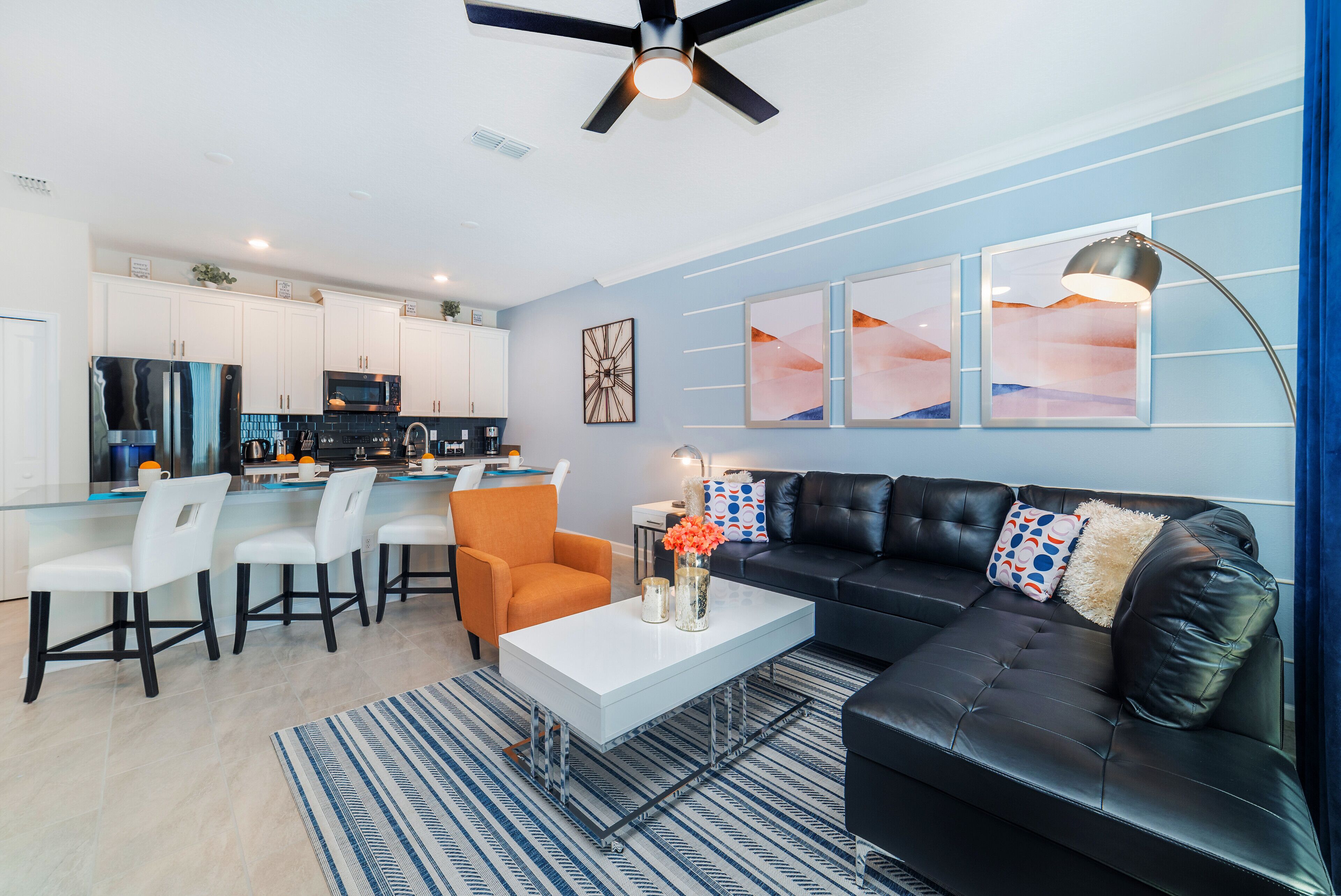 A modern living room with a black leather sofa, white chairs, a coffee table, and artwork on the wall.