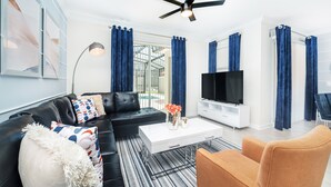 Un salon moderne avec un canapé en cuir noir, une table basse blanche et un téléviseur posé sur un meuble blanc.