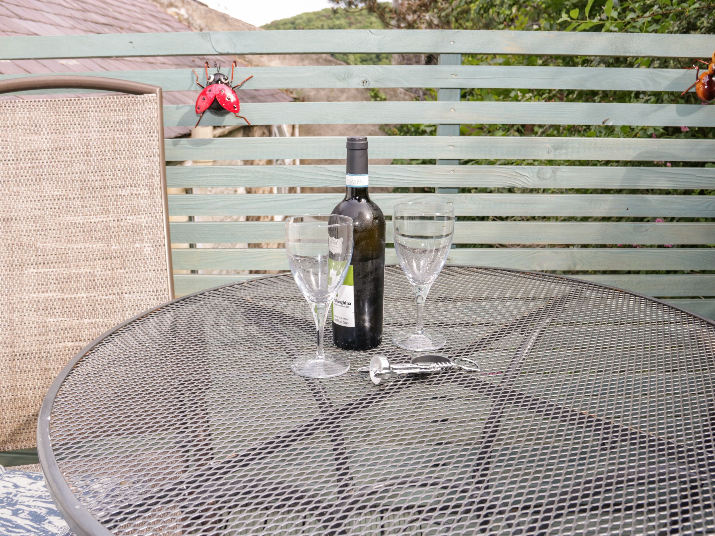 A round metal table with a bottle of wine and two empty wine glasses.