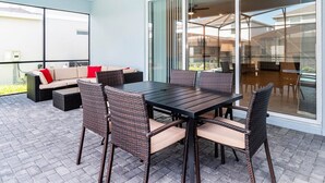 An outdoor patio with a table and chairs, a sofa, and a glass door leading to a covered area. - Last Minute Disney! Private Pool, Hot Tub & Themed Bedrooms. Book Now! #49467 (Orlando)