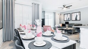 Un comedor moderno con una mesa larga lista para una comida, un sofá y un televisor al fondo.