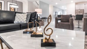 Ein modernes Wohnzimmer mit einem Marmortisch, einem schwarzen Sofa mit gemusterten Kissen und einer eleganten Küche im Hintergrund.