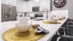 Eine moderne Küche mit weißen Schränken, Edelstahlgeräten und einer langen Arbeitsplatte mit goldenen Tischsets und weißen Geschirr.