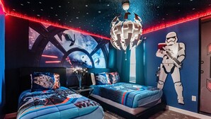 Un dormitorio con dos camas, ropa de cama con temática de Star Wars, un casco de Star Wars en la pared y una lámpara de araña con temática de Star Wars.