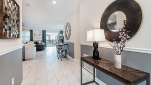 Una cocina moderna con una isla central, un comedor con una mesa redonda y sillas, y una sala de estar con sofá y decoración mural.