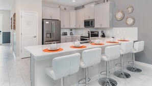 Una cocina moderna con armarios blancos, electrodomésticos de acero inoxidable y una isla central con taburetes de bar.