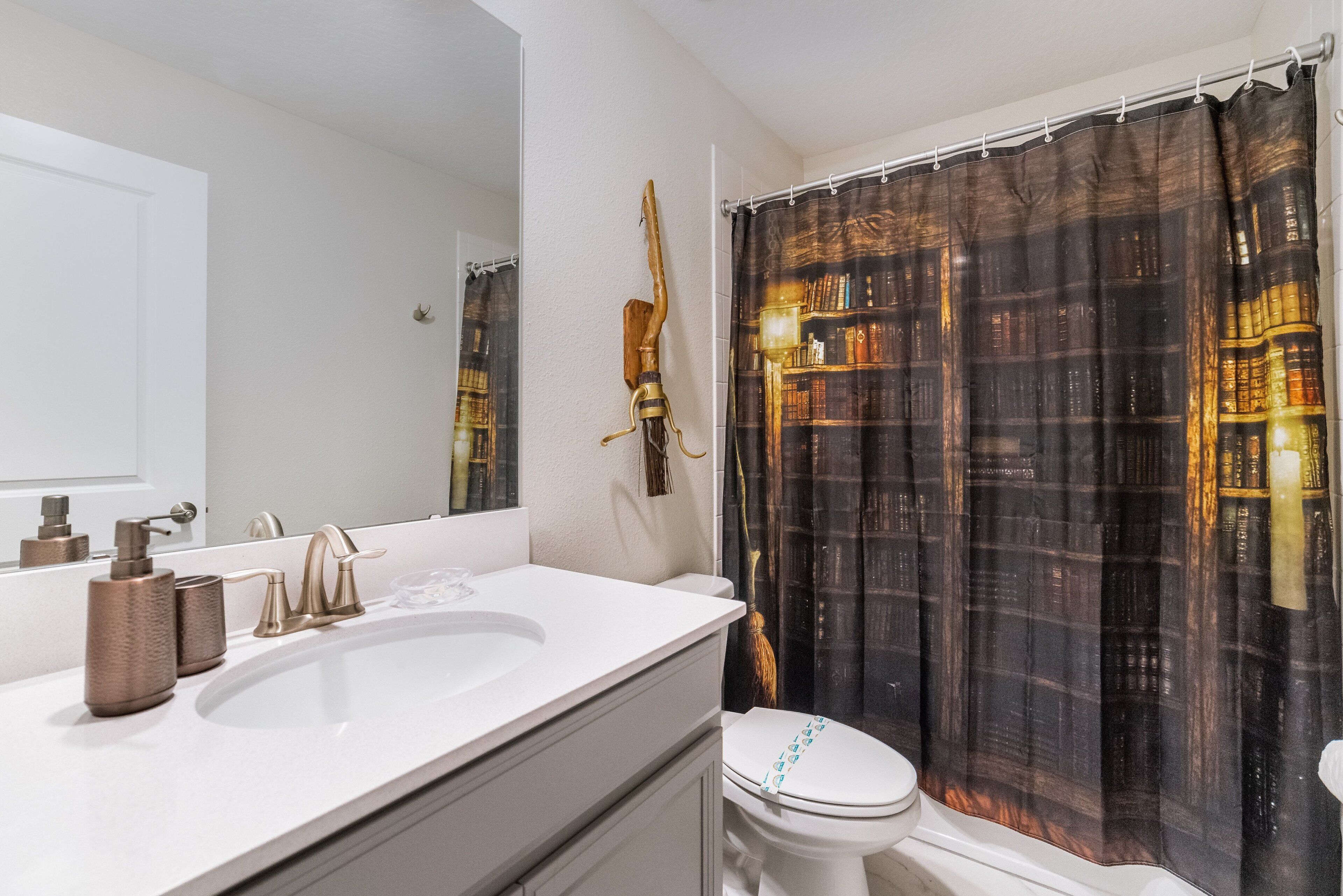 A bathroom with a white sink, a mirror, a toilet, and a shower curtain with a book pattern.