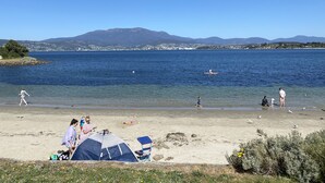 Una playa con tiendas de campaña, cielo despejado y montañas al fondo.