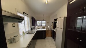 Cocina compacta con estufa, lavamanos y refrigerador, que incluye un ventanal con persianas y una lámpara colgante.