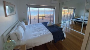 Un dormitorio con una cama grande, una mesita de noche, un espejo y vistas a la playa.