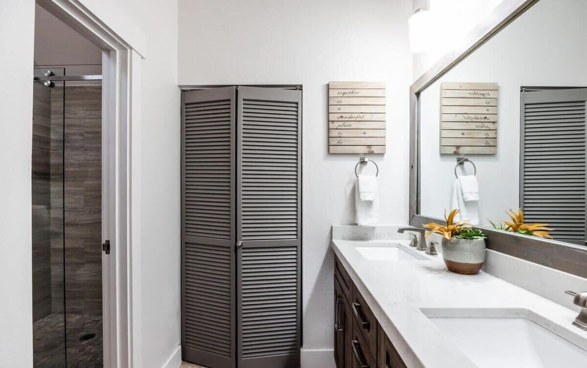 A modern bathroom with a glass shower enclosure, a wooden cabinet, a sink with a plant, and a mirror with a towel rack.