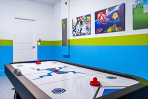 Uma mesa de bilhar com parede listrada em verde e azul, uma porta branca e obras de arte com tema do Mario.