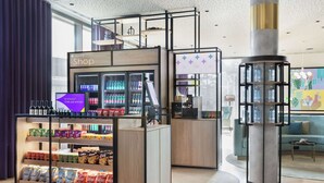 Una zona commerciale moderna con un negozio 'Spark Shop' dotato di area refrigerata, corsia per snack e esposizione di acqua in bottiglia.