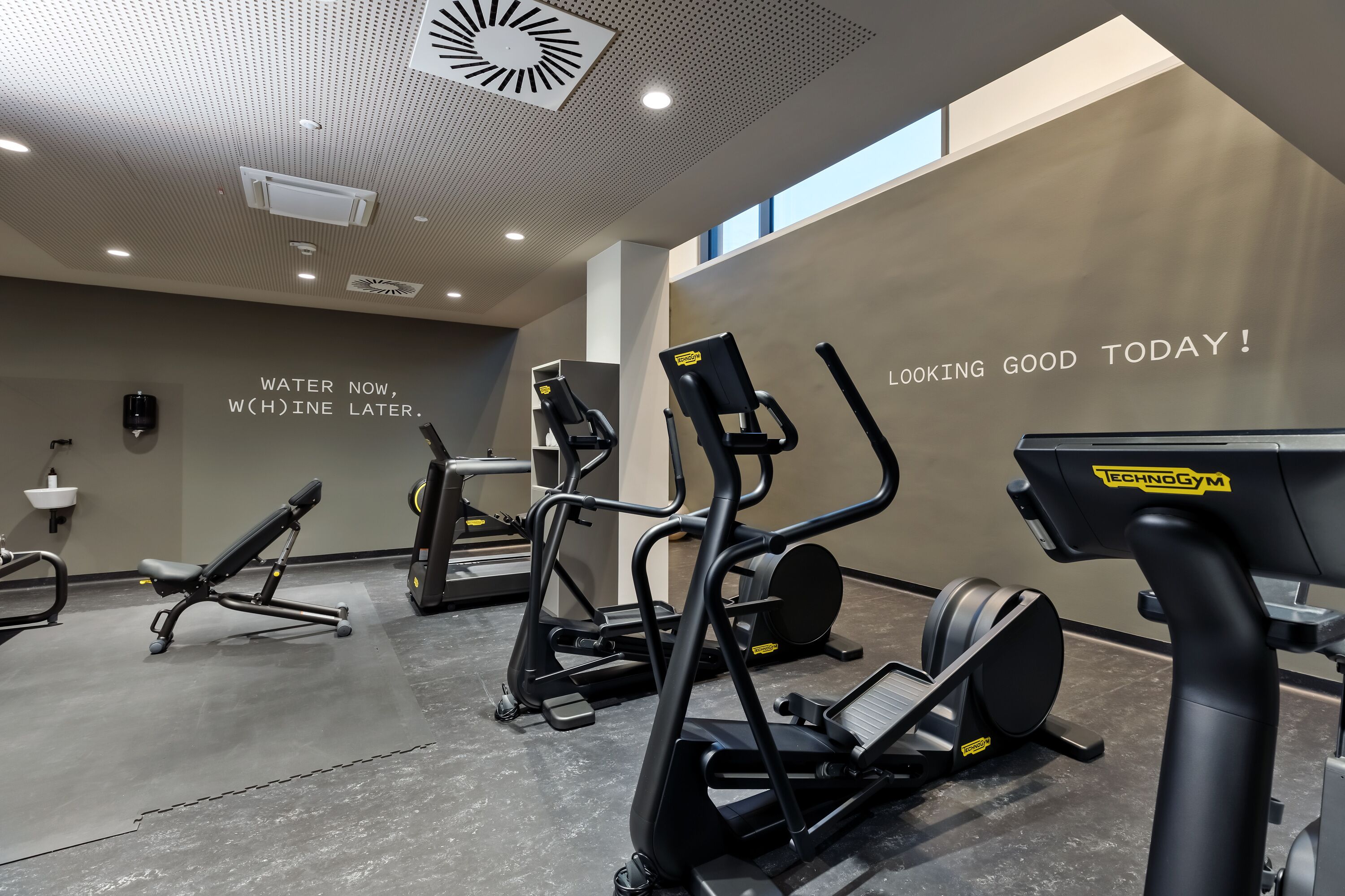 Un gimnasio moderno con diversos equipos de ejercicio, mensajes motivacionales en la pared y un interior limpio y bien iluminado.