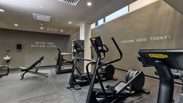 Un gimnasio moderno con diversos equipos de ejercicio, mensajes motivacionales en la pared y un interior limpio y bien iluminado.