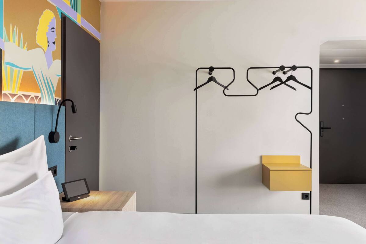 A hotel room with a bed, bedside table, and a wall-mounted coat rack.