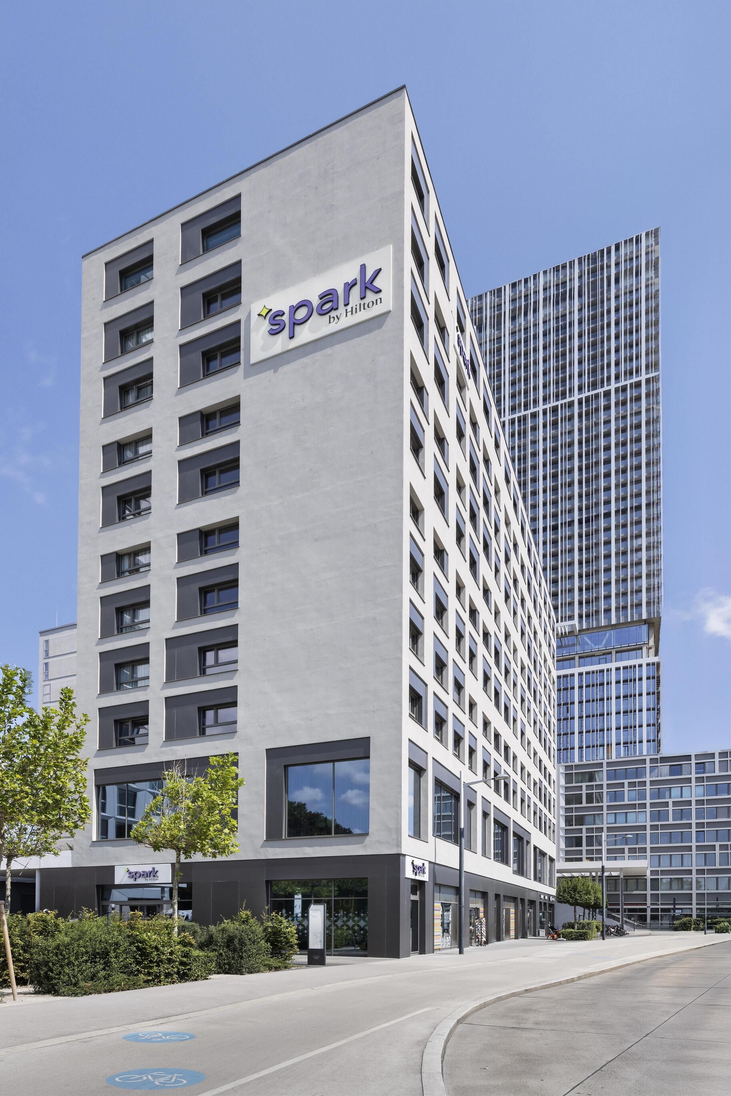 A modern hotel building with a 'spark by Hilton' sign, featuring a clean, rectangular facade with multiple windows and a flat roof.