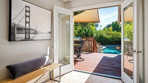 A room with a bench, a framed picture of the Golden Gate Bridge, and a view of a backyard with a pool and outdoor furniture. - The Elm House: Private Pool, Hot Tub, Napa Getaway (Napa)