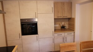 A modern kitchen with light-colored cabinets, a built-in oven, and a wooden dining table with chairs. - Apartment Julius 4 - nice, quiet and in the middle - (Sankt Andreasberg)