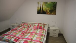 A bedroom with a bed, two bedside tables, and a painting of a forest on the wall. - Apartment Julius 4 - nice, quiet and in the middle - (Sankt Andreasberg)