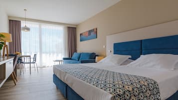 A hotel room with a large bed, a desk with a chair, a sofa, and a large window with curtains.