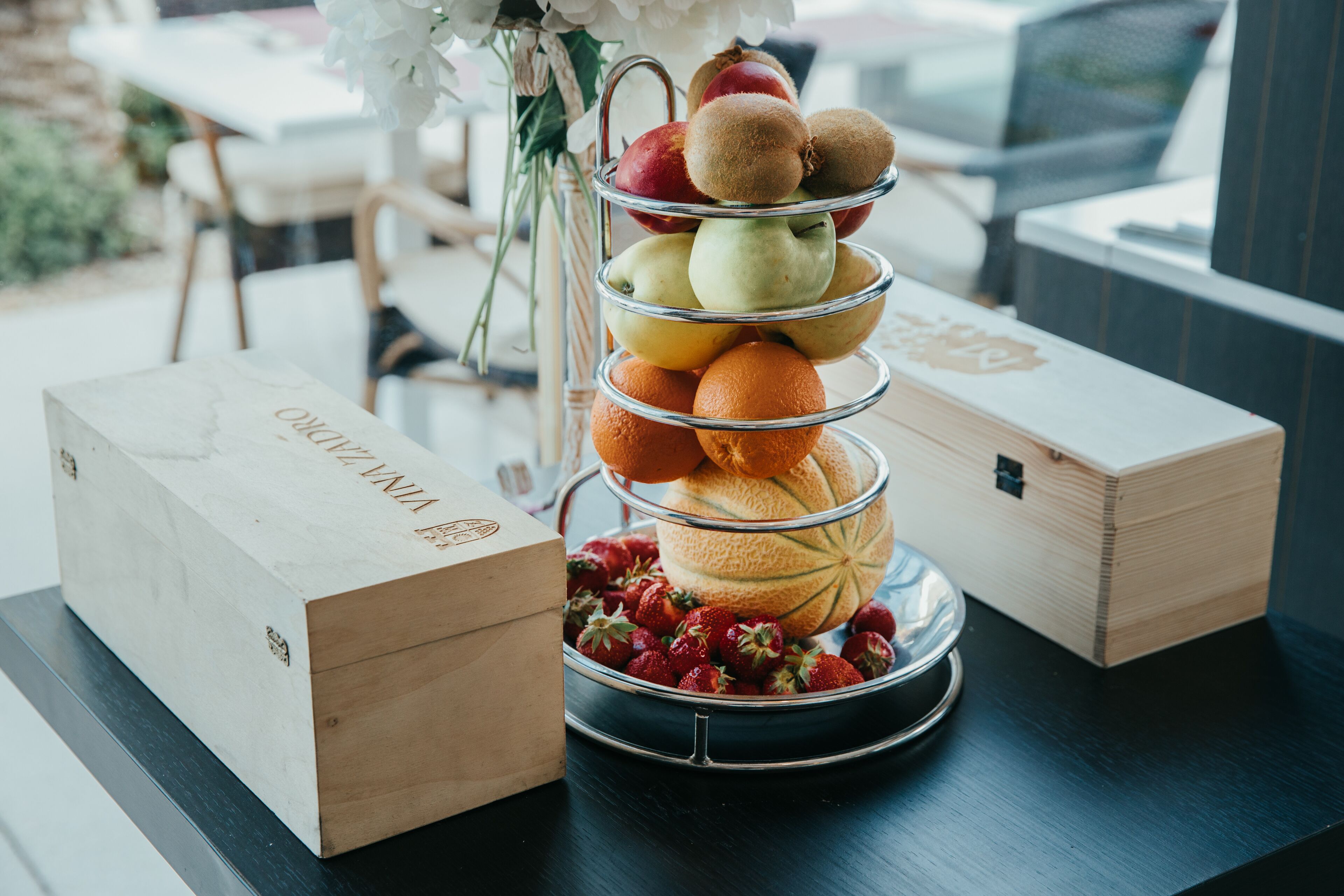 Un présentoir à fruits à plusieurs niveaux, avec des pommes, des poires, des oranges et des fraises, posé sur une table.