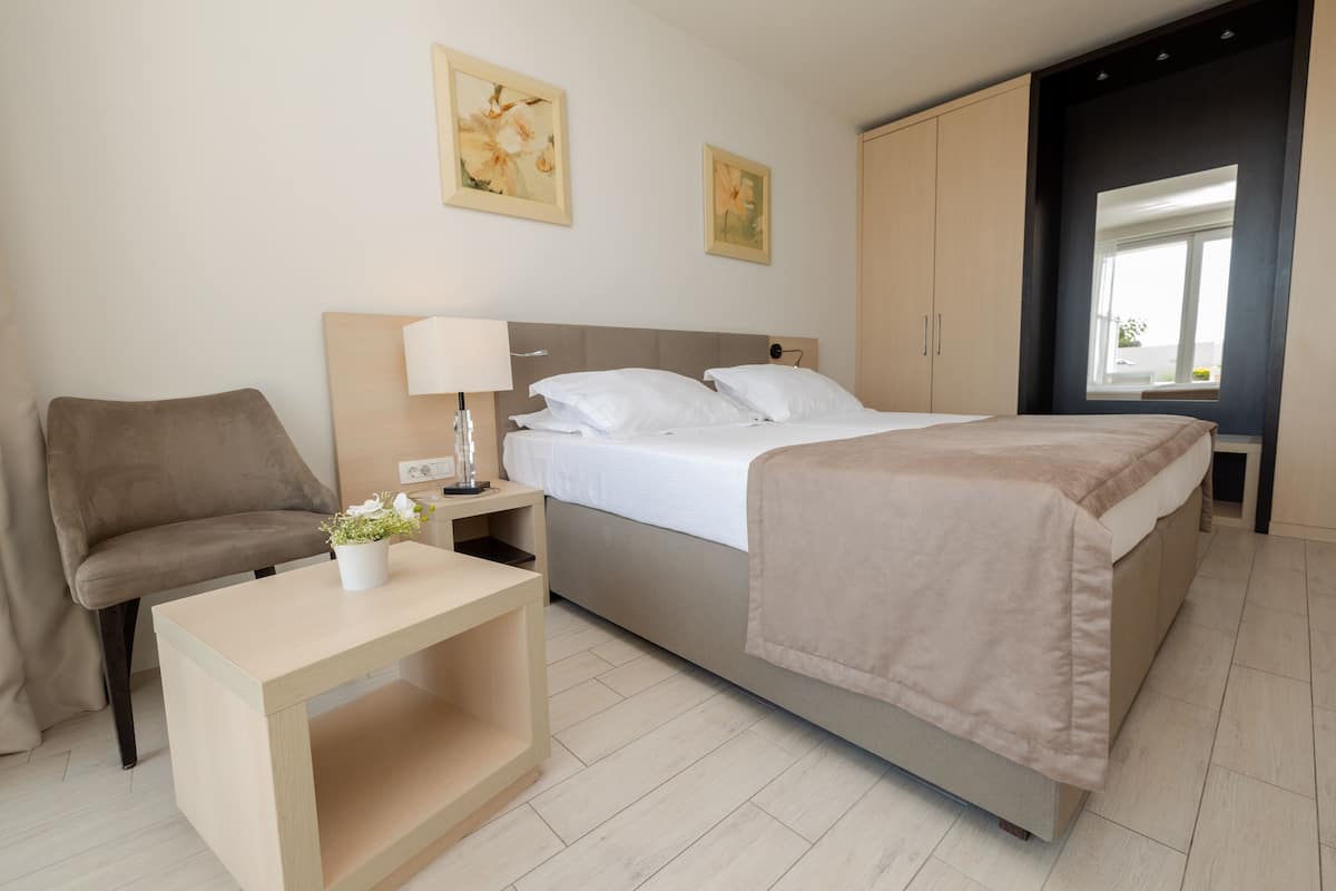 Een slaapkamer met een bed, nachtkastje, lamp en een stoel.