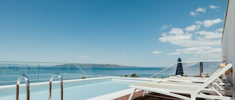 A pool area with lounge chairs and a glass railing overlooking the sea.