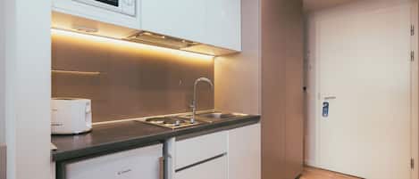 A compact kitchen with a microwave, toaster, sink, and a door with a lock.