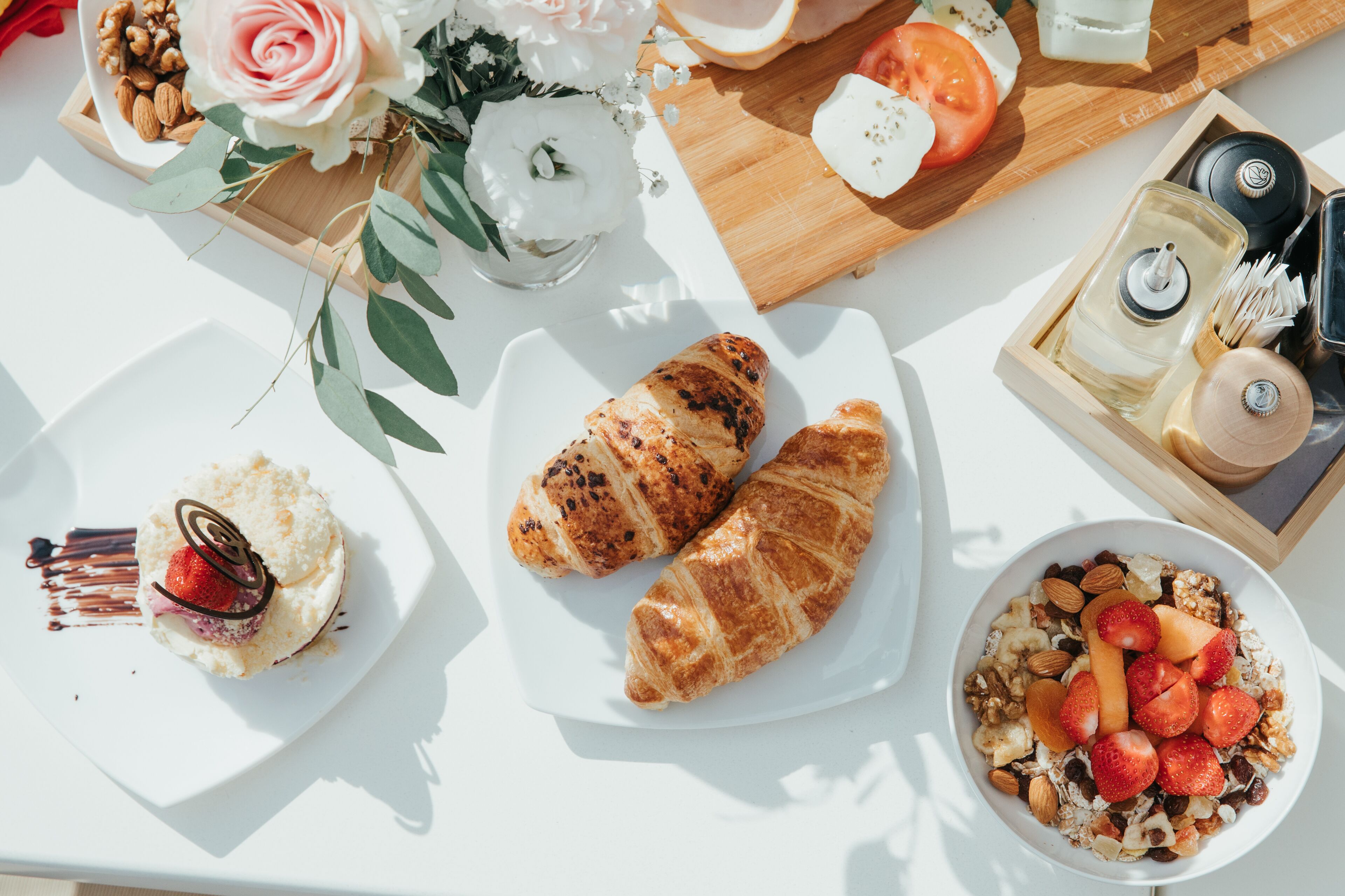 Ein Frühstückstisch mit Croissants, ein Dessert mit Erdbeeren und eine Schüssel Müsli mit Früchten und Nüssen.