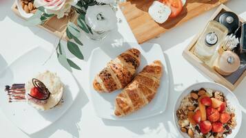 Ein Frühstückstisch mit Croissants, ein Dessert mit Erdbeeren und eine Schüssel Müsli mit Früchten und Nüssen.
