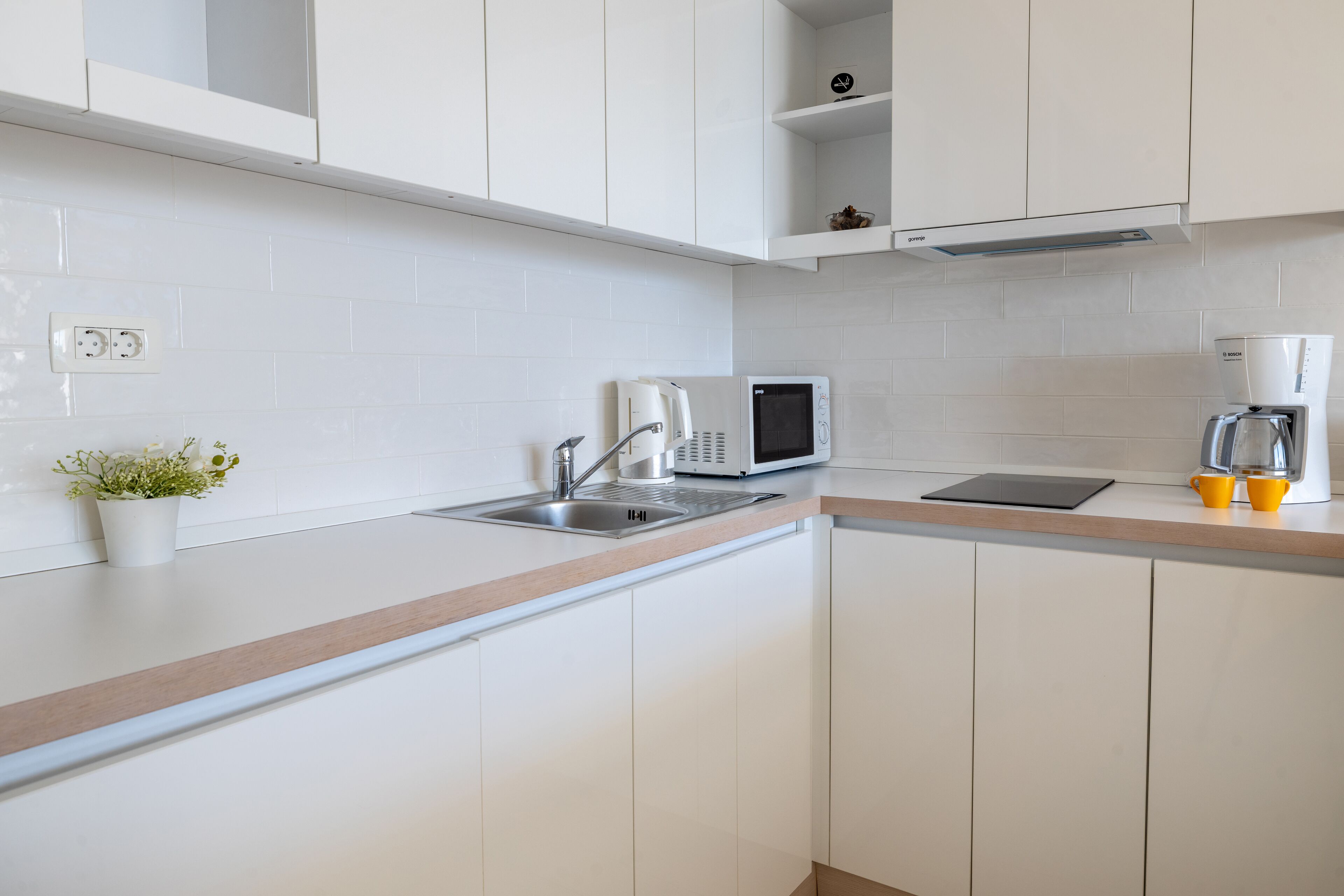 A modern kitchen with white cabinets, a stainless steel sink, a microwave, and a coffee maker.