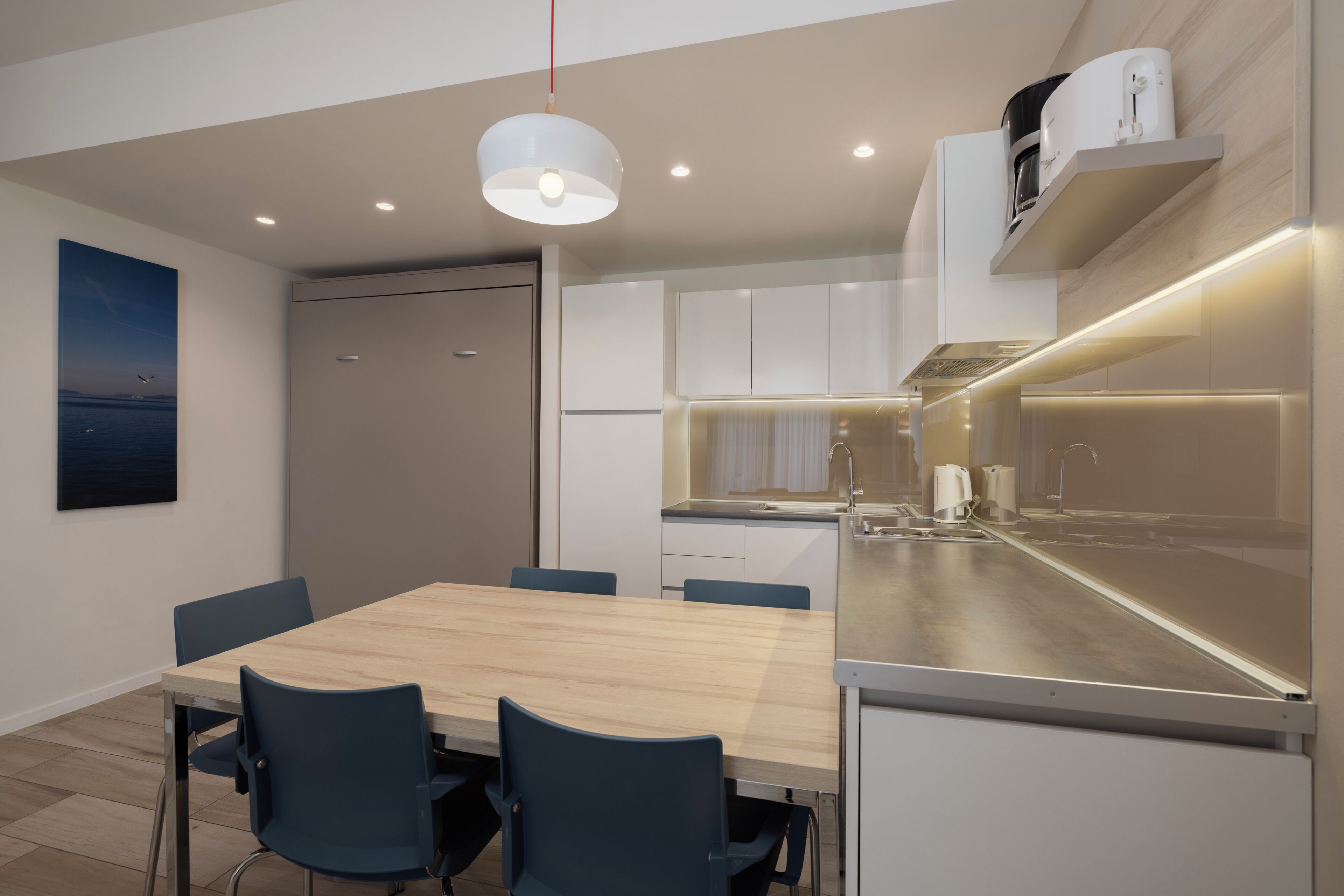 Una cocina moderna con armarios blancos, una mesa de comedor de madera y sillas azules.