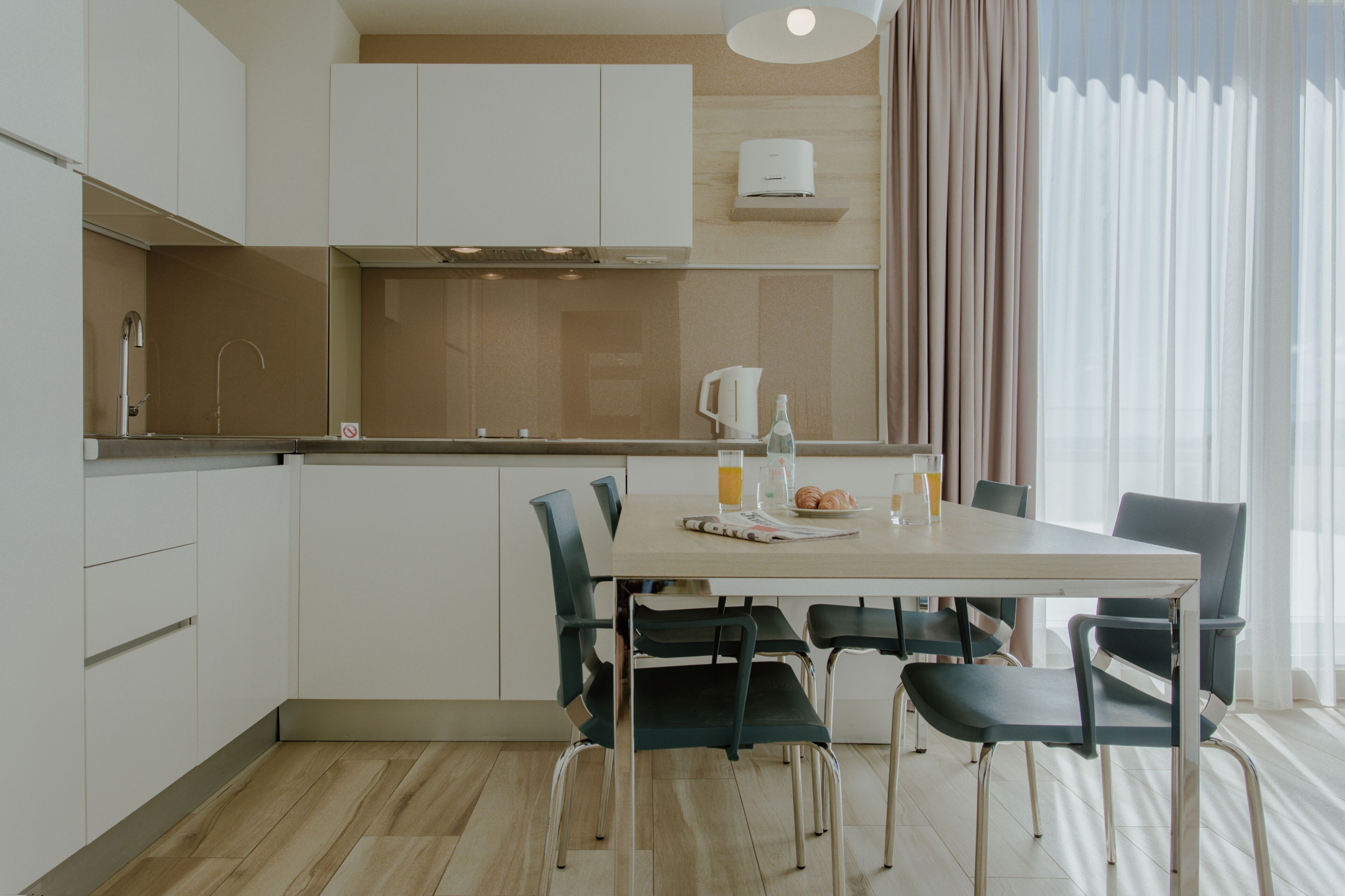 A modern kitchen with white cabinets, a stainless steel sink, and a dining area with a table and chairs.