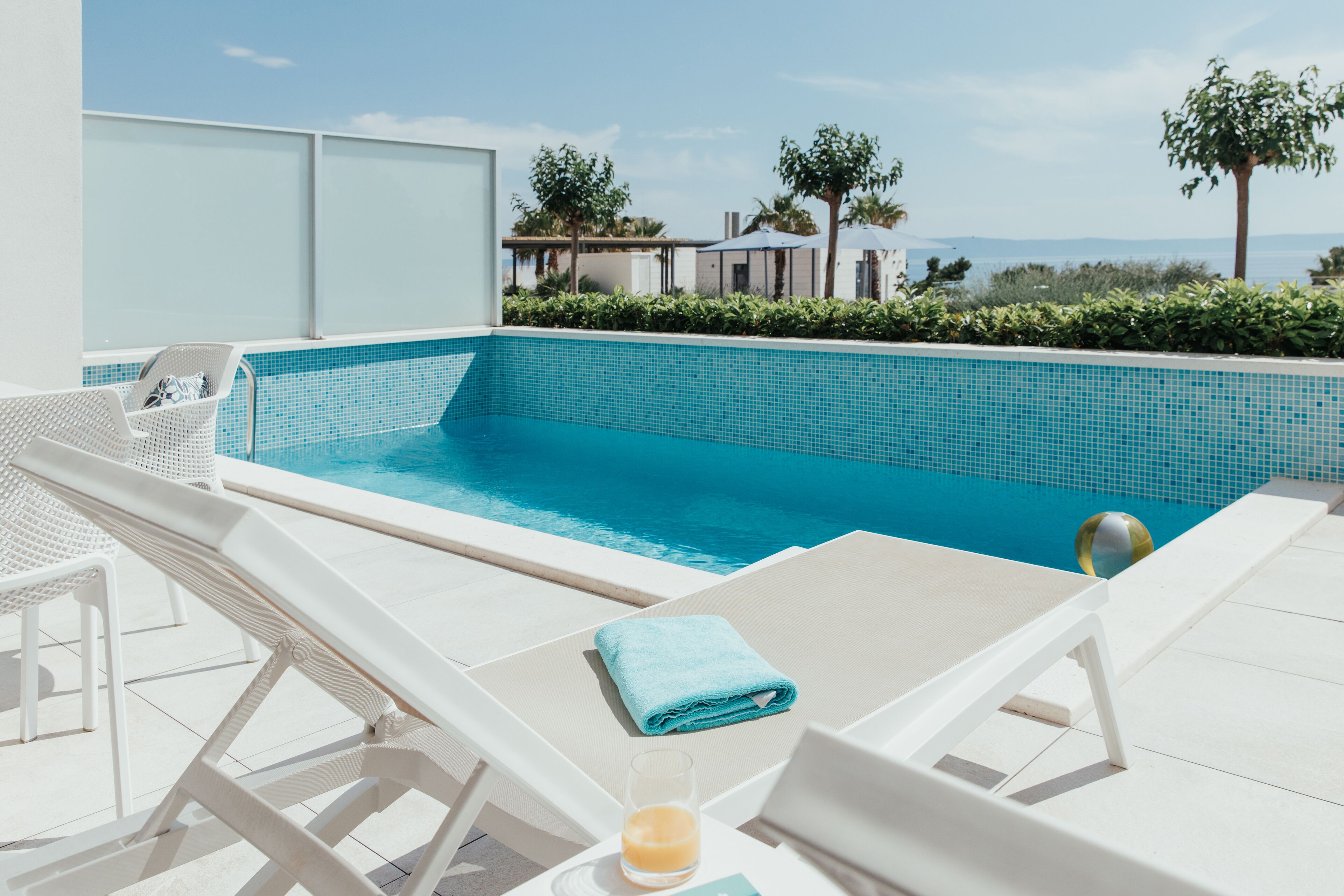 Zona de piscina con sillones de descanso y un vaso de jugo de naranja.