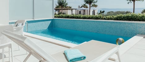 Zona de piscina con sillones de descanso y un vaso de jugo de naranja.