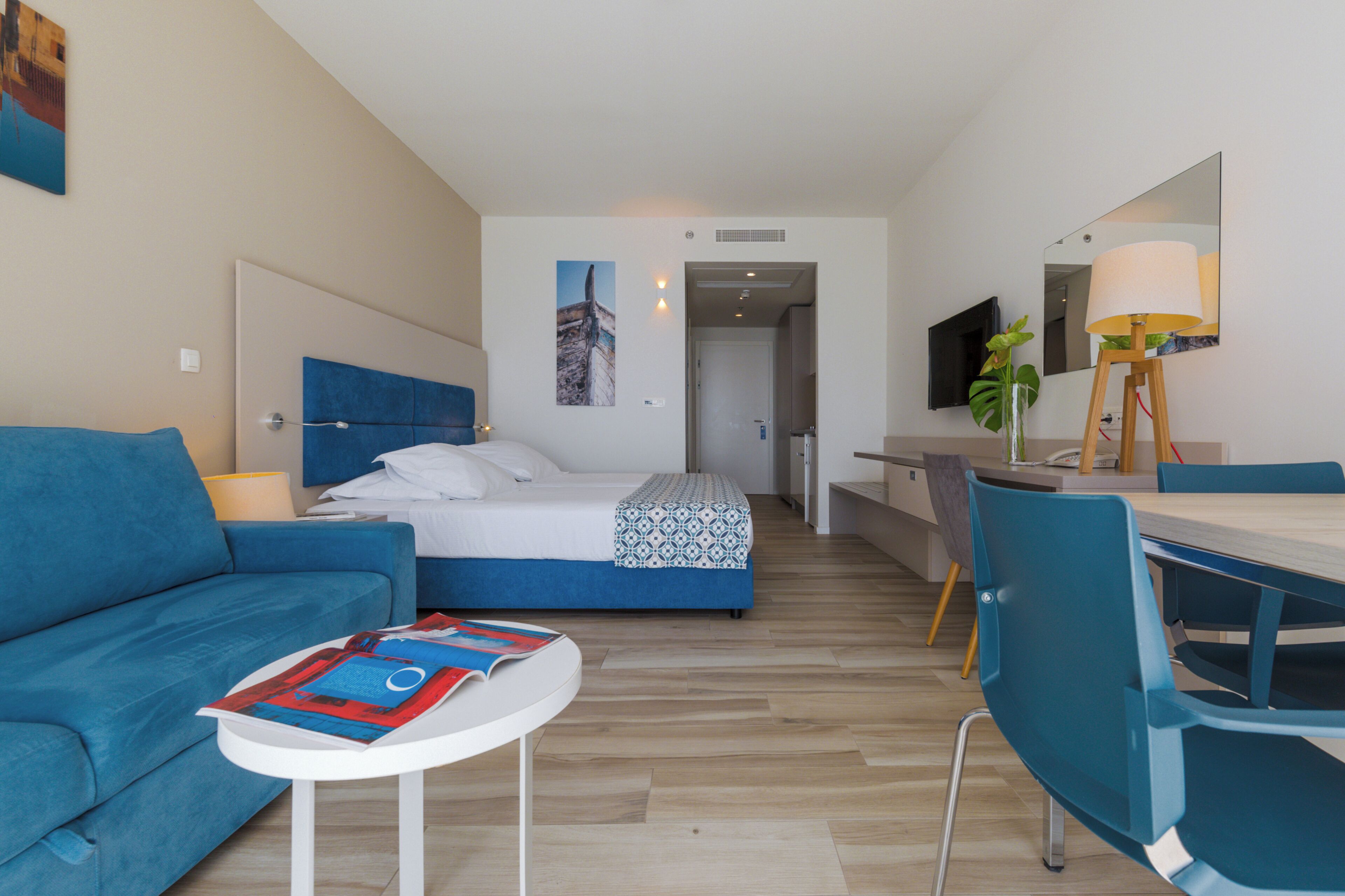 Ein modernes Hotelzimmer mit einem Bett, einem blauen Sofa, einem Schreibtisch und einem Sessel.