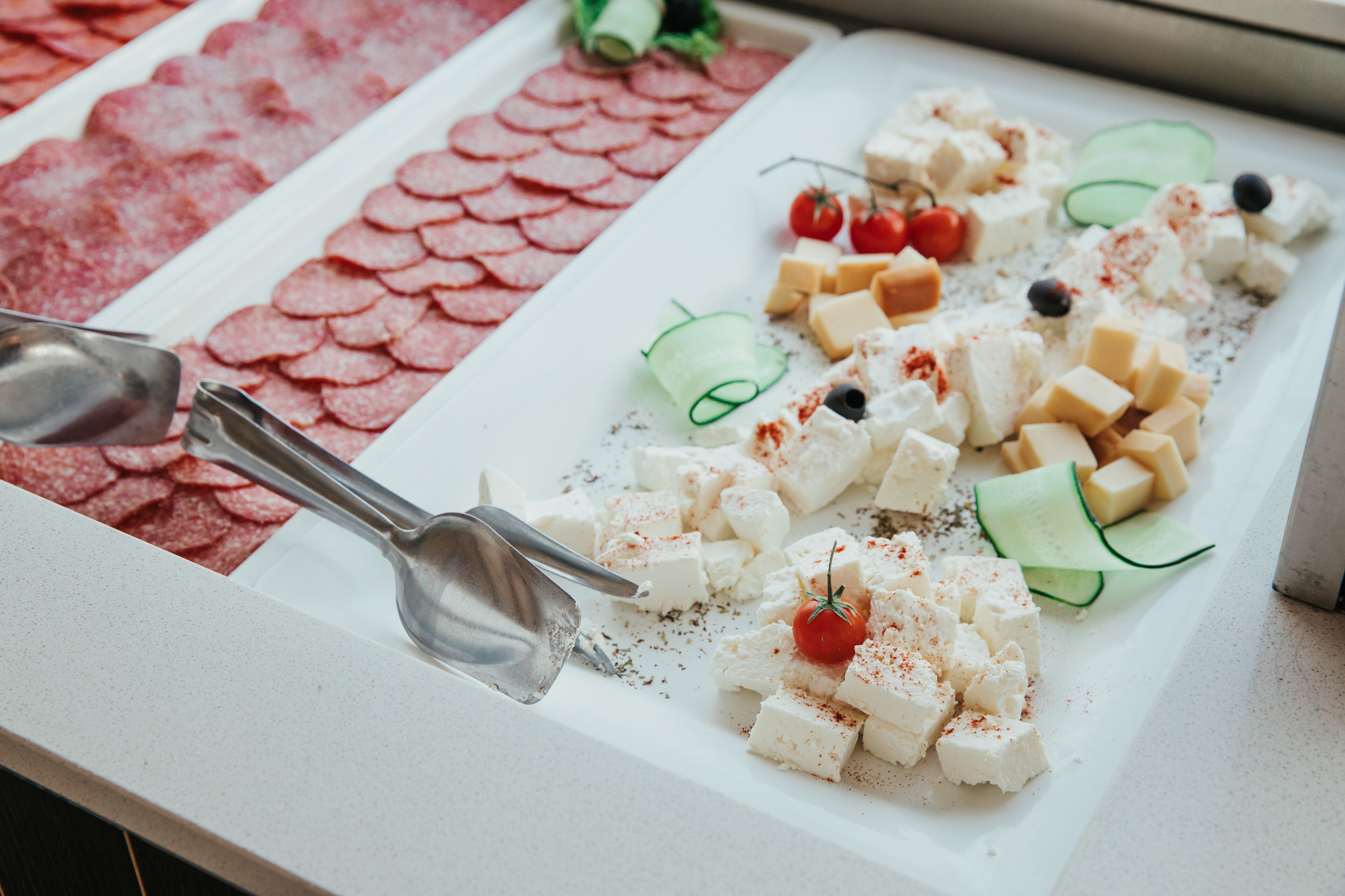 A buffet with various food items including cheese, tomatoes, cucumbers, olives, and sliced meats.