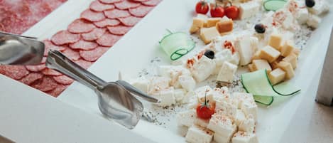 A buffet with various food items including cheese, tomatoes, cucumbers, olives, and sliced meats.