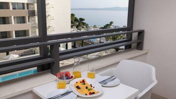A balcony with a table set for breakfast, a view of the sea, and a pool in the background.