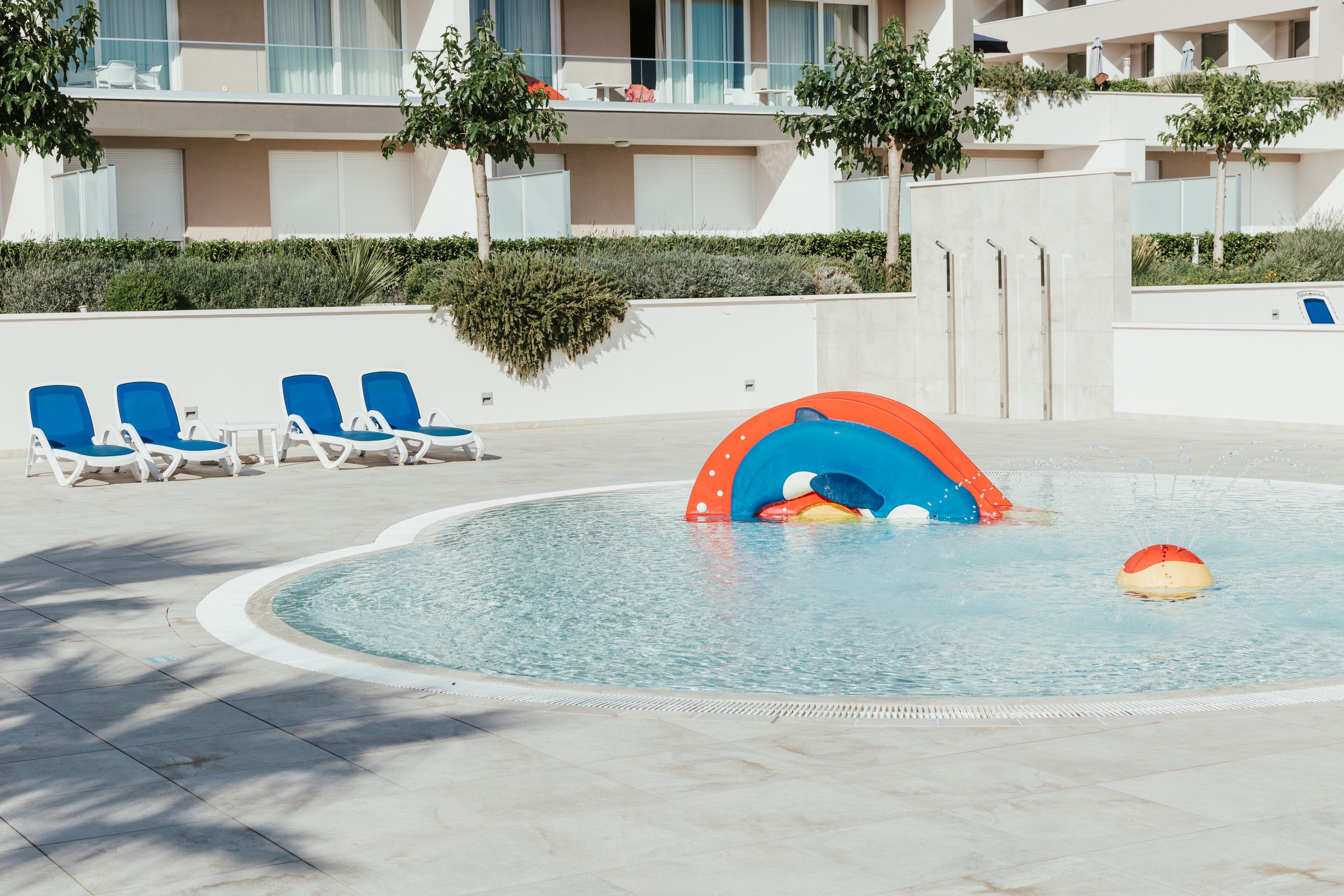 Une piscine avec des chaises longues bleues et un espace de jeux aquatiques coloré.