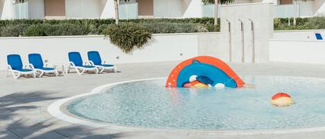 A swimming pool with blue lounge chairs and a colorful water play area.