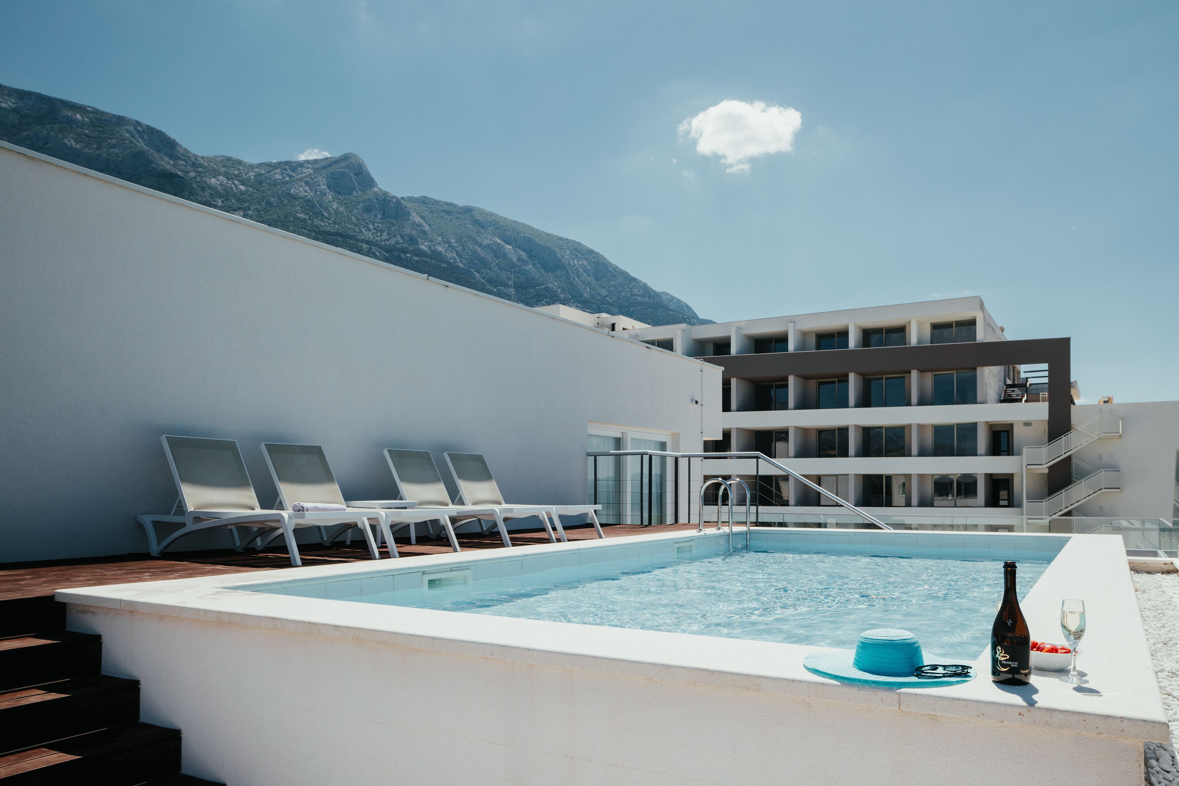 A pool area with lounge chairs, a bottle of champagne, and a glass on a table.