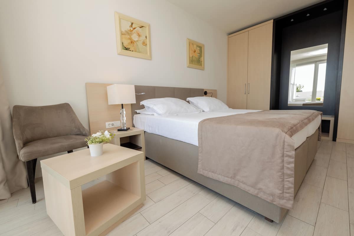 Een slaapkamer met een bed, nachtkastje, lamp en een stoel.