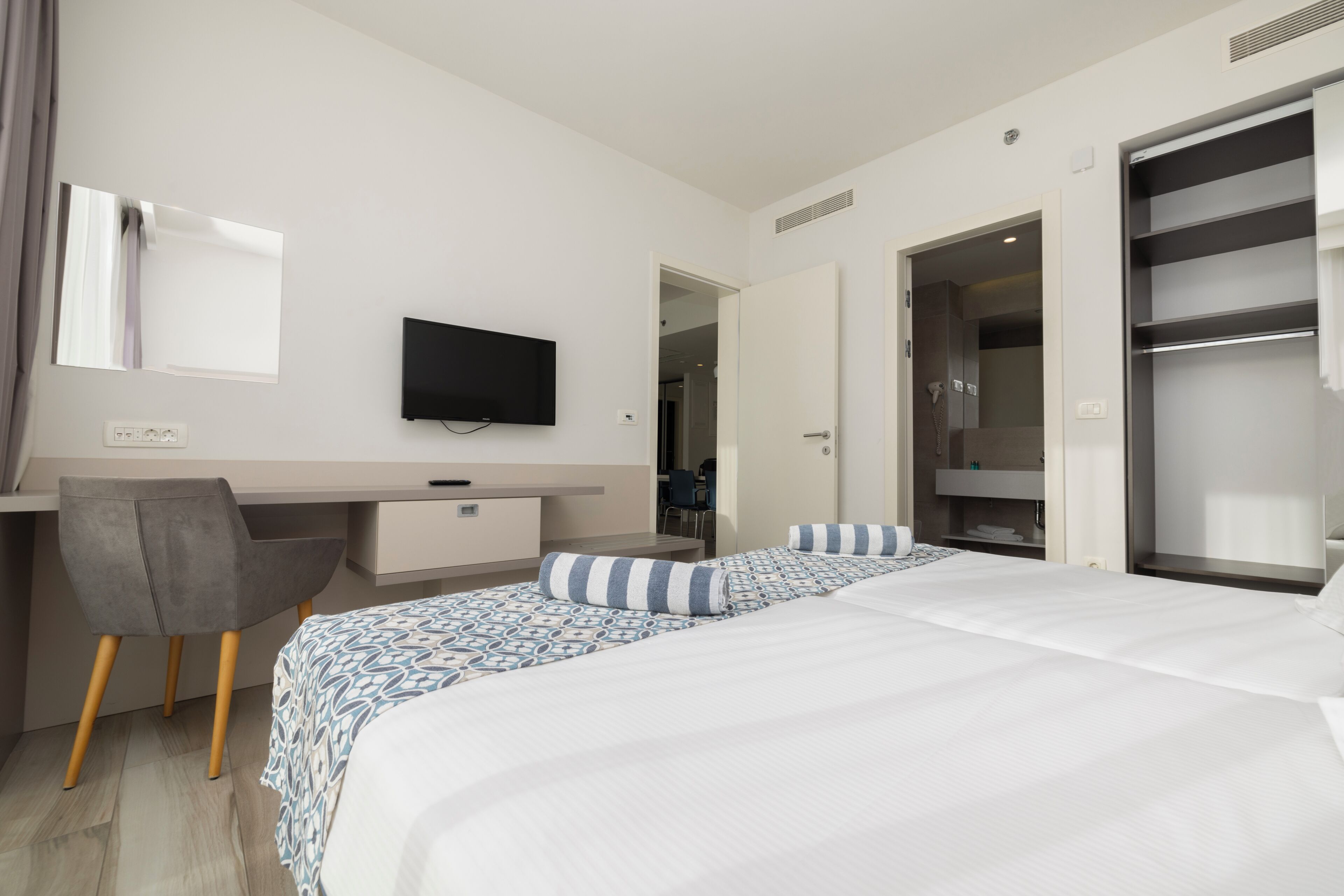 A hotel room with a bed, a desk, a chair, a TV, and a wardrobe.