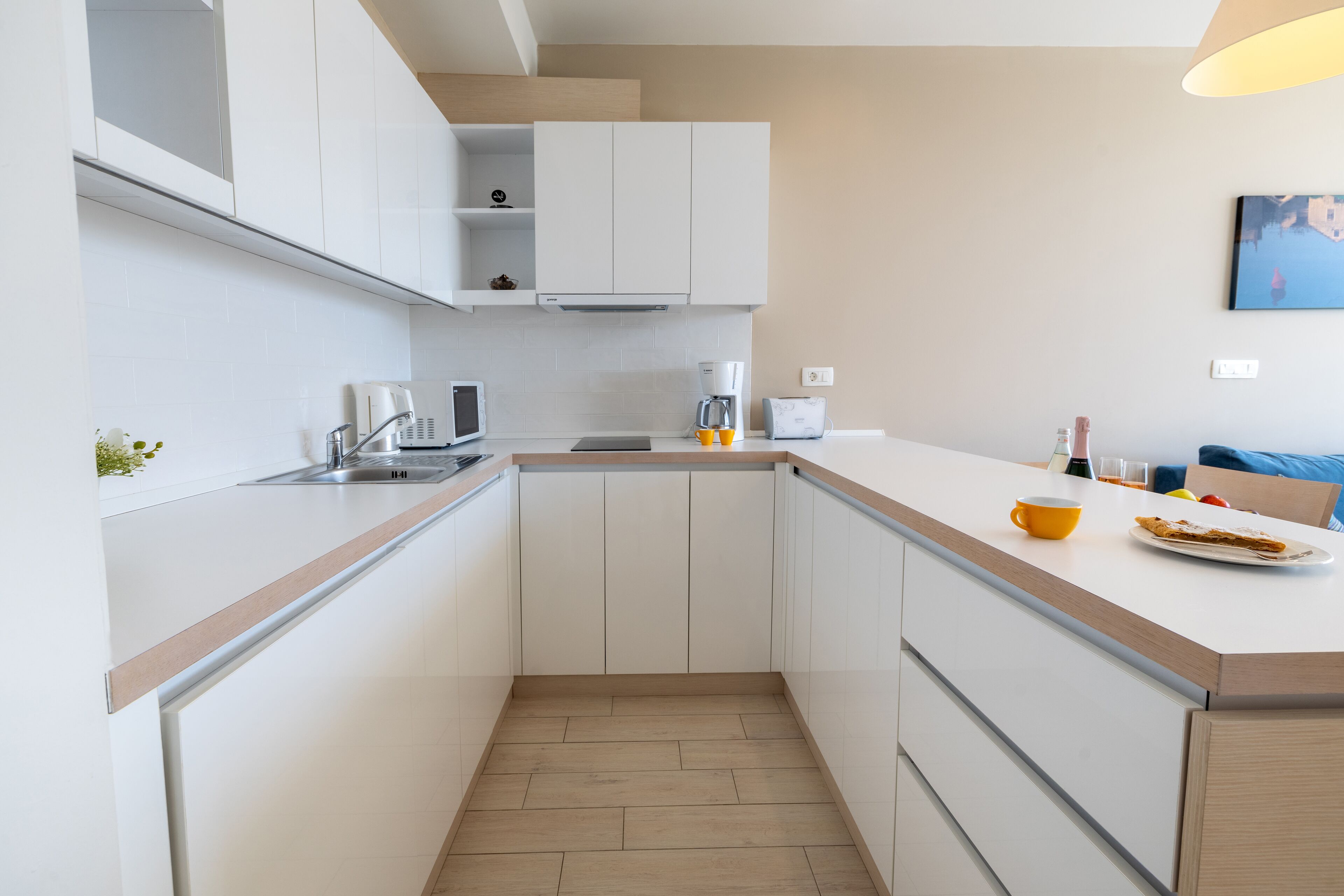 A modern kitchen with white cabinetry, a wooden countertop, and a small dining area with a table and chairs.